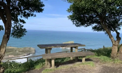 Imagen de un banco en el inicio del camino del Mirador de Andrín con el Islote de Castro Ballota al fondo.