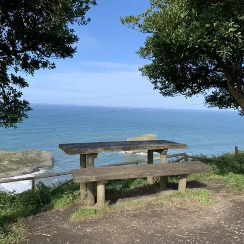 Imagen de un banco en el inicio del camino del Mirador de Andrín con el Islote de Castro Ballota al fondo.