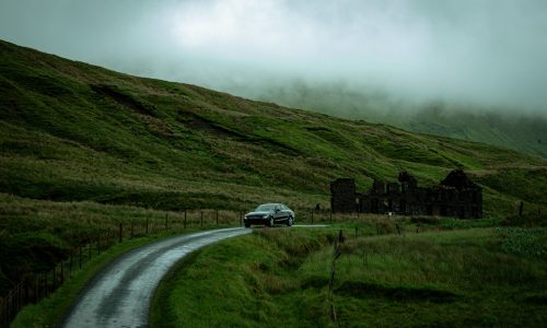 Coche circulando por una carretera mojada entre colinas verdes con niebla